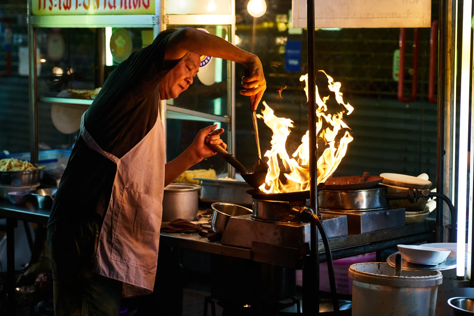 A Bangkok street food vendor cooking to order at a busy evening stall