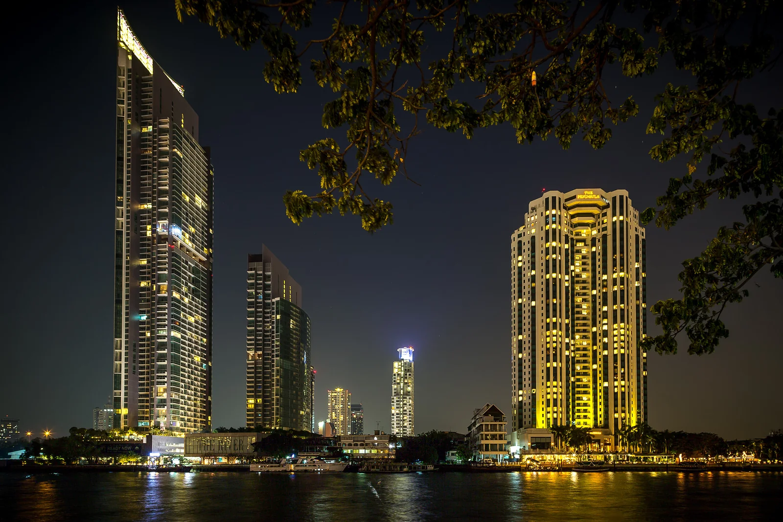 Chao Phraya River at night with illuminated Bangkok riverside buildings, as seen from the Bang Rak bank