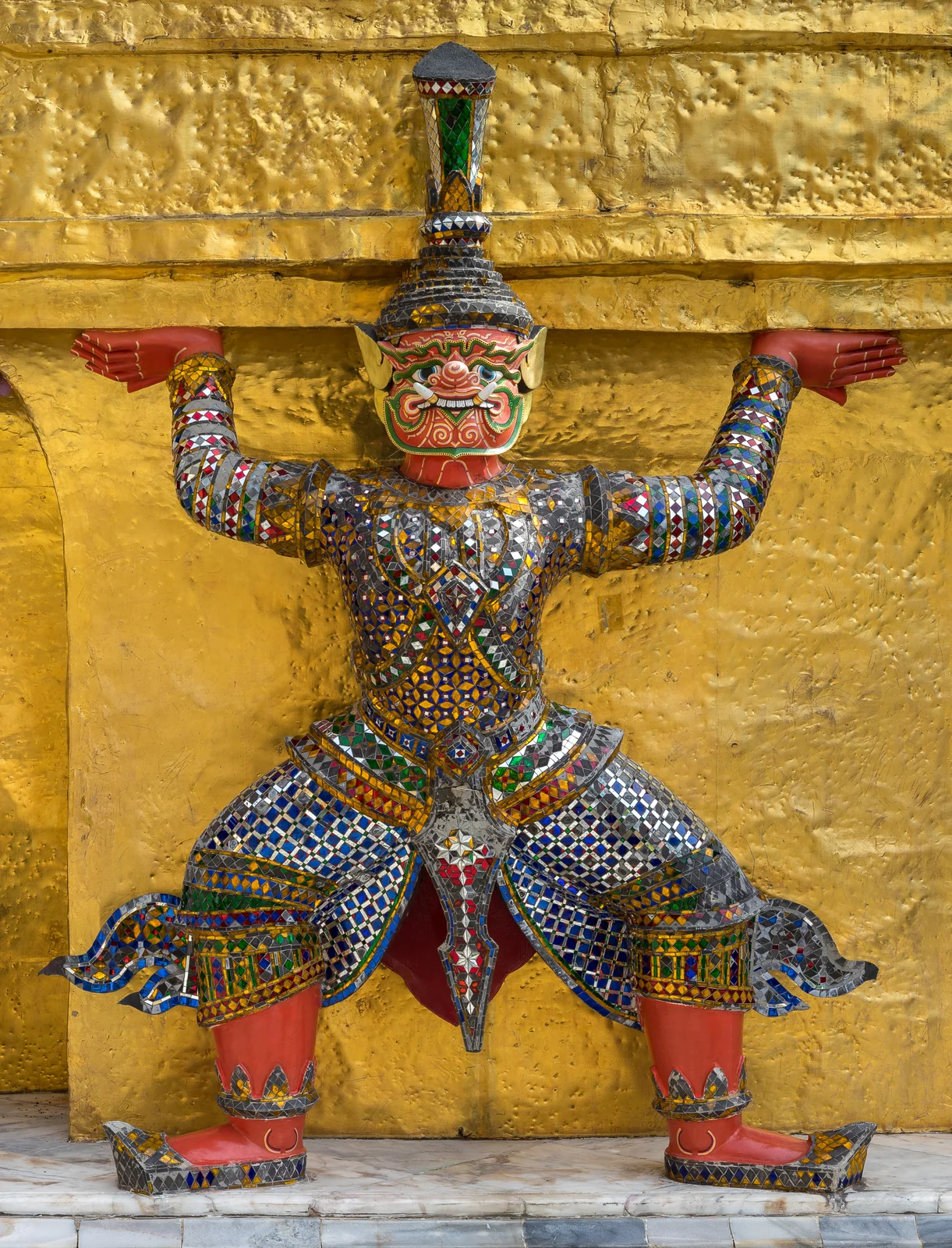 Mirrored yaksha guardian statue holding up the base of a gilded Thai temple chedi