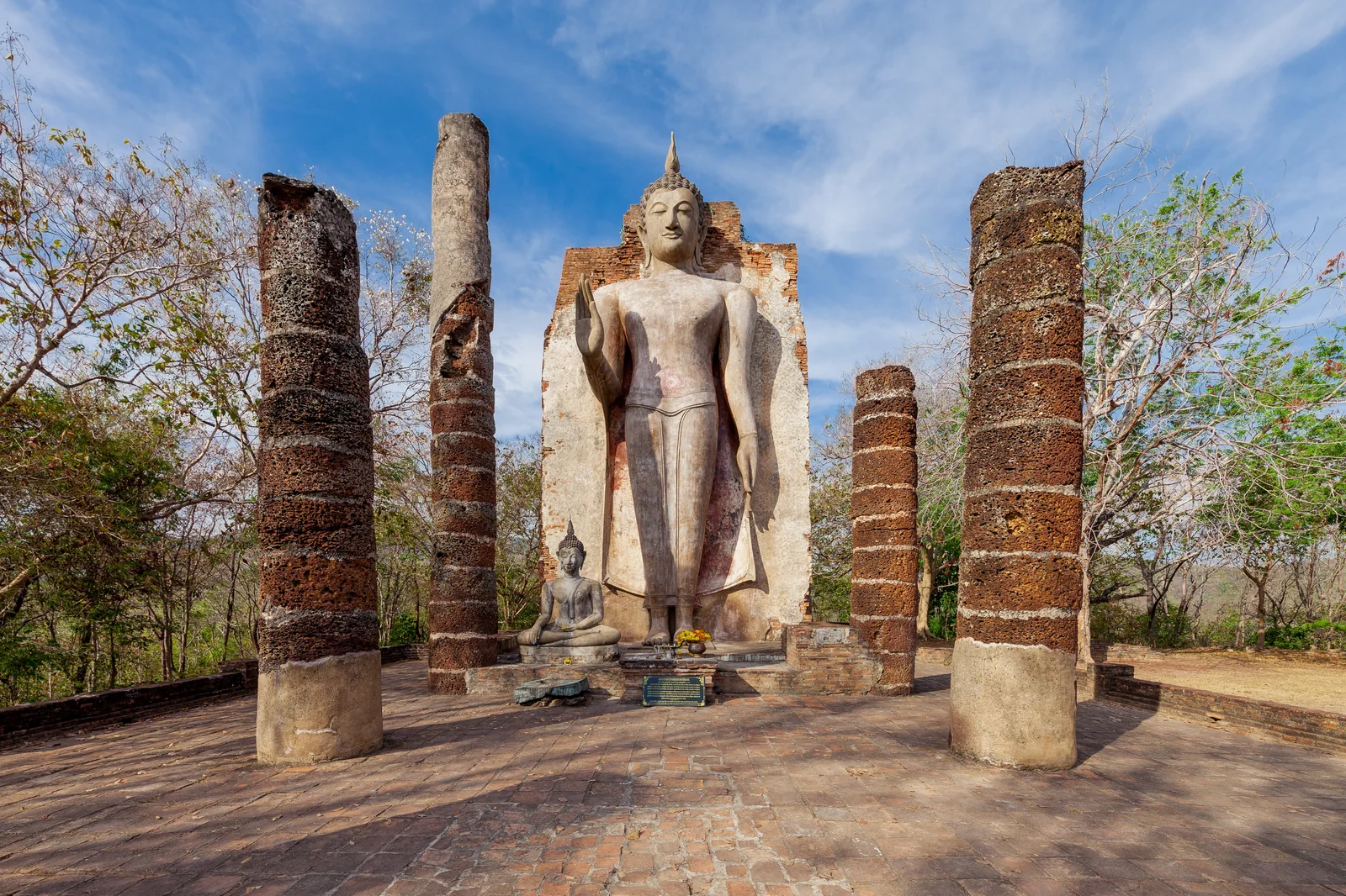 Standing Buddha between laterite columns at Sukhothai Historical Park under a blue sky