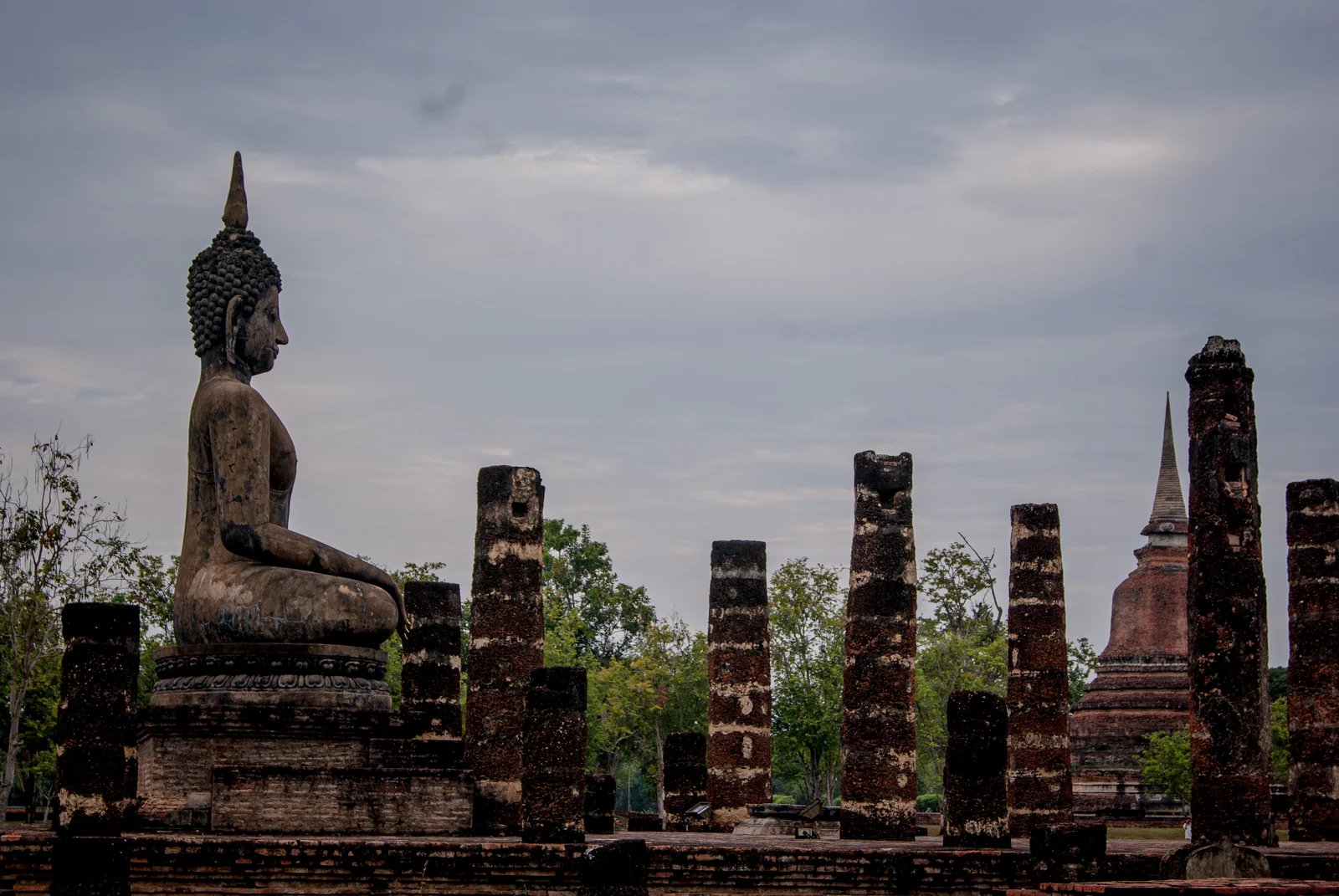 Seated Buddha image and brick columns among the ruins of Wat Mahathat, Sukhothai, Thailand
